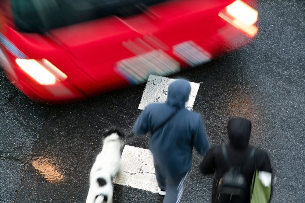 Aerial view of a speeding red car passing dangerously close to pedestrians crossing a wet crosswalk in Wisconsin representing driver negligence and liability in a pedestrian accident claim