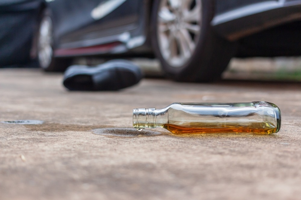 Spilled liquor bottle lying on the ground beside a damaged vehicle at a drunk driving accident scene