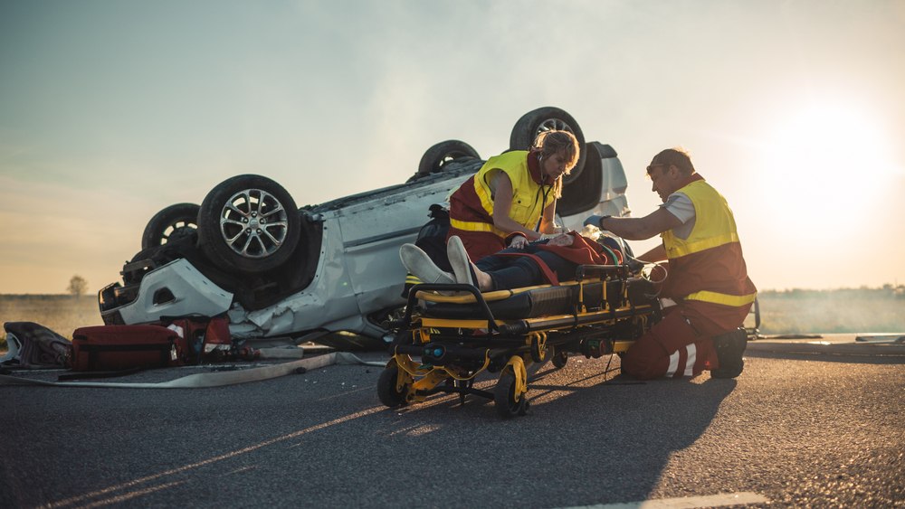 Paramedics treating an injured patient on a stretcher beside an overturned vehicle after a catastrophic injury accident