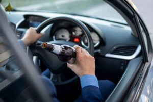 Man driving while holding a beer bottle, representing a Milwaukee drunk driving accident case