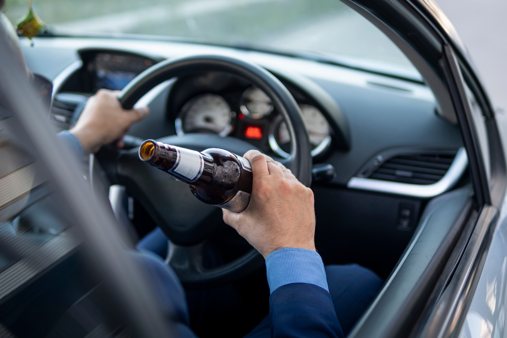 Man driving while holding a beer bottle, representing a drunk driving accident case