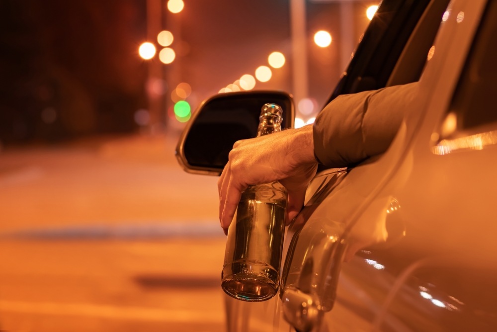 Hand holding a beer bottle out of a car window while driving at night, illustrating a dram shop liability case